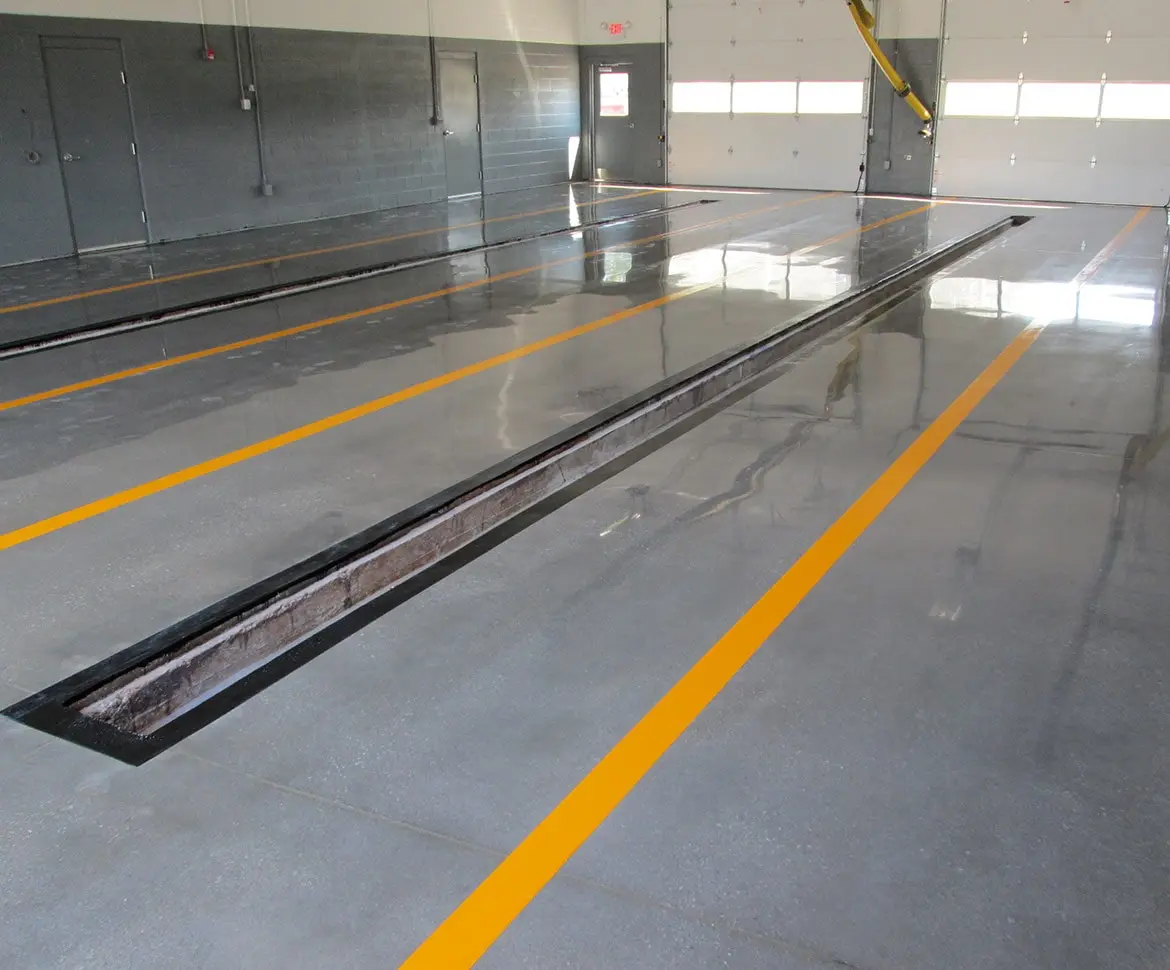 Grey epoxy coated industrial garage floor with orange lane lines and central drain channel