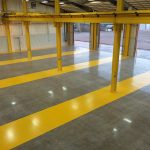 Interior of a large, empty industrial warehouse in Broward with polished concrete floors featuring wide yellow stripes and support columns, high ceilings, and large windows letting in natural light.