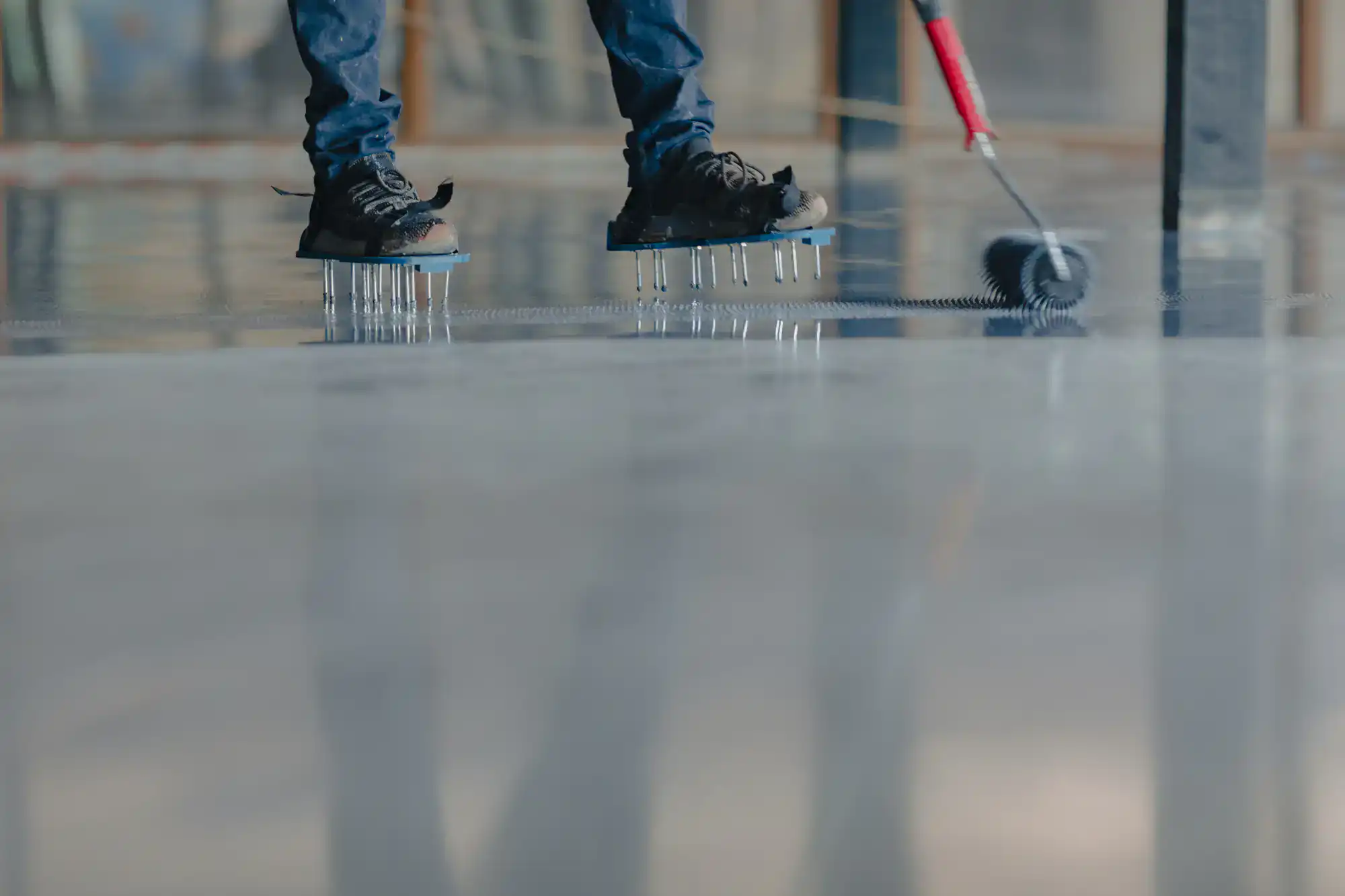 A person wearing spiked shoes is standing on a wet floor while using a roller to spread epoxy or resin coating across the surface in Broward and Miami-Dade County.