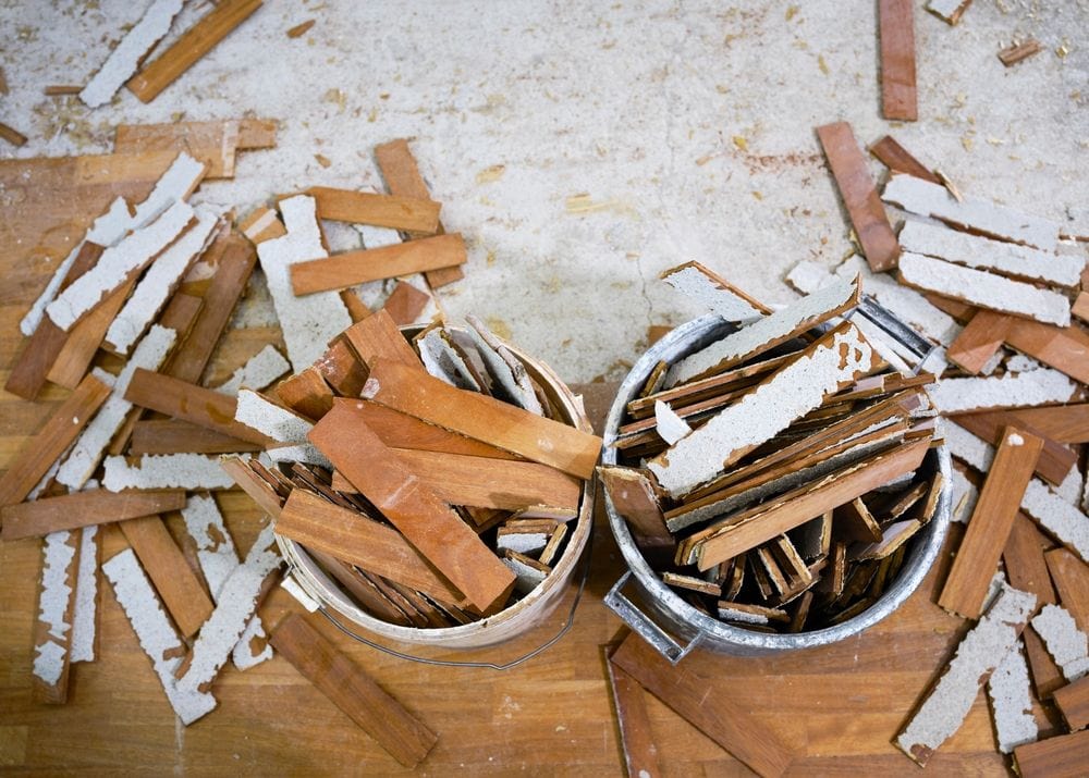 Two buckets filled with broken wood and debris sit on a floor scattered with more pieces of damaged wood and plaster, indicating demolition or renovation work in progress in Broward and St. Lucie County, FL.
