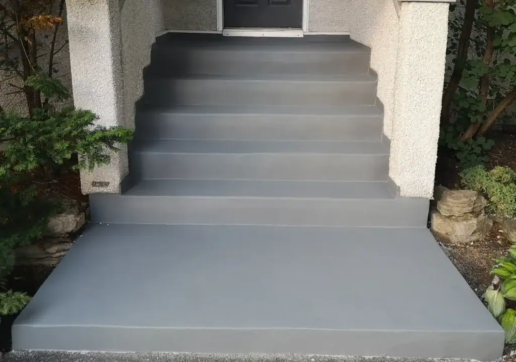 A set of six smooth, gray concrete steps leads up to a front door, with a wide matching landing and greenery on both sides.