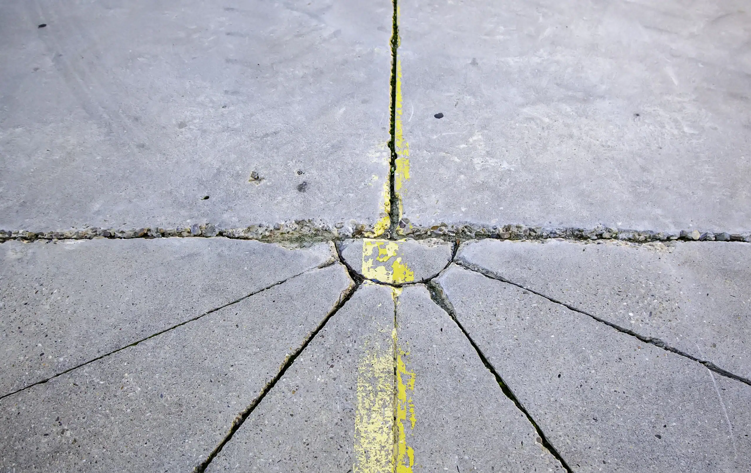 A concrete surface with multiple cracks converging at a circular point, intersected by a faded yellow line running vertically through the center.
