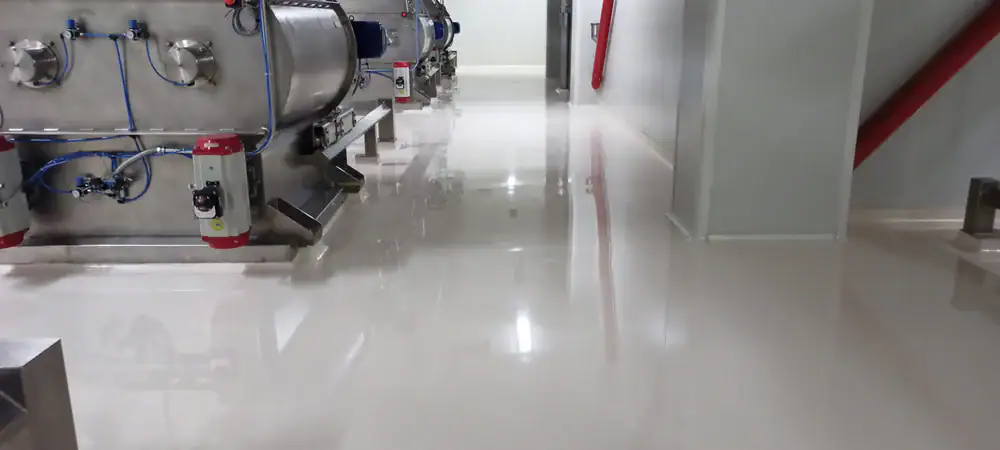 A clean, shiny industrial floor with stainless steel equipment along the walls and red fire extinguishers attached to machines in a well-lit facility.