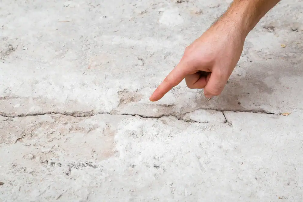 A hand points to a long, visible crack in a concrete surface, highlighting damage or wear on the floor.